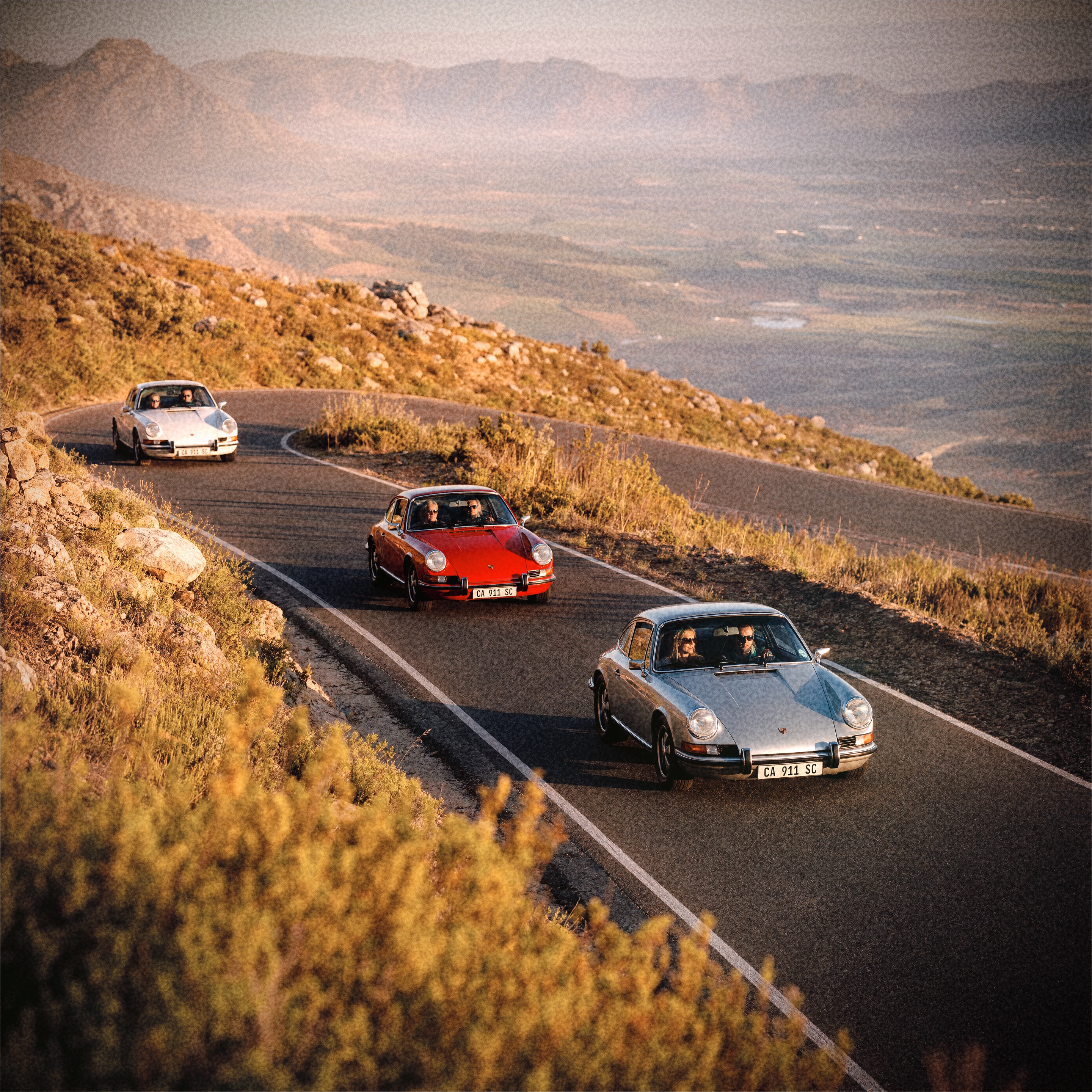 Three classic Porsche 911s on a Cape mountain pass at golden hour